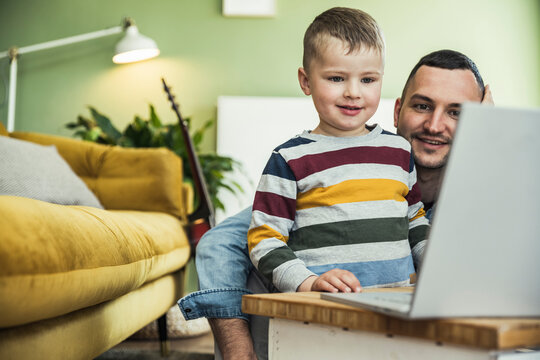 Smiling father with cute son watching video on laptop in living room at home