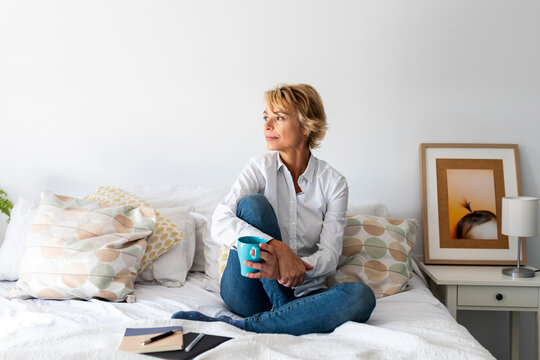 Relaxed mature woman sitting on bed at home