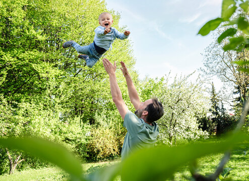 Happy father throws his smiling son into the air in a green garden