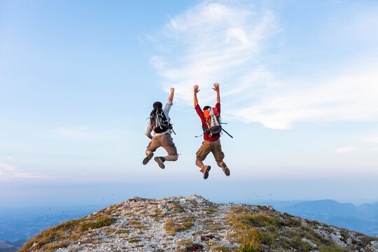 Italy, Monte Nerone, two happy and successful hikers jumping on top of a mountain