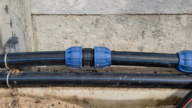 Close-up of black HDPE water pipes with blue compression coupling fittings installed along a concrete wall at a building construction site