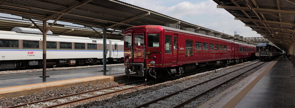 A red Royal Blossom train stands on the tracks at Hua Lamphong railway station alongside a white Kiha 183 and a blue SRT Prestige carriage in Thai capital Bangkok
