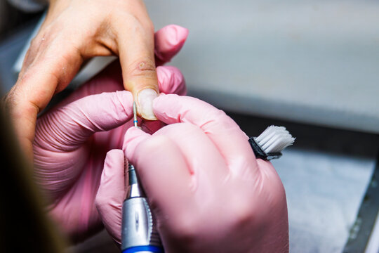 Manicurist performing professional nail care with a nail drill in a beauty salon