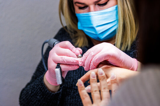 Manicurist wearing mask and gloves performing nail care on a client's hand