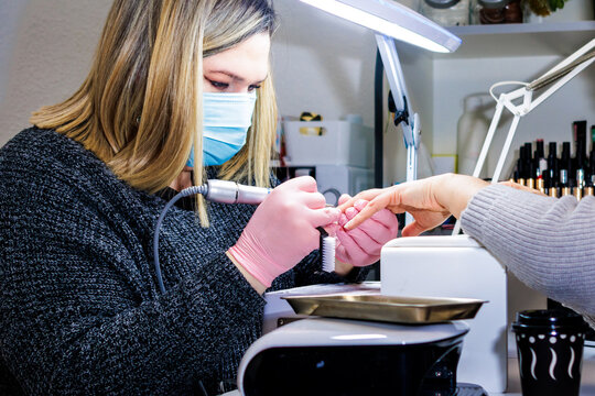 Manicurist applying nail drill on client's fingernails in a professional beauty salon