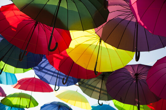 Colorful umbrellas forming a dense overhead canopy outdoors, vibrant decorative display, creative background, summer festival.