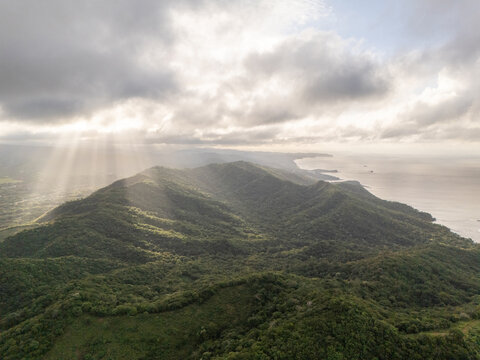 Aerial view of the lush green hills and coastline with sun rays breaking through the clouds over the Pacific Ocean in San Juan del Sur, Rivas, Nicaragua.