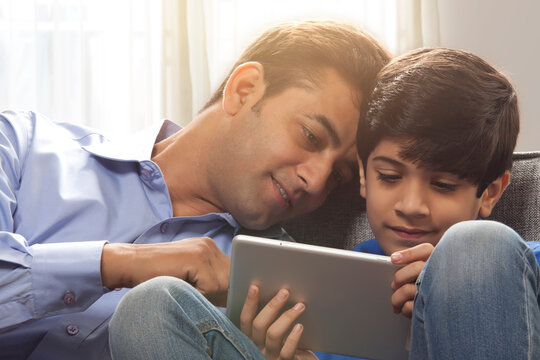 
Father and son watching at digital tablet on couch
