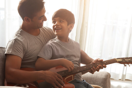 Father and son playing guitar sitting on sofa