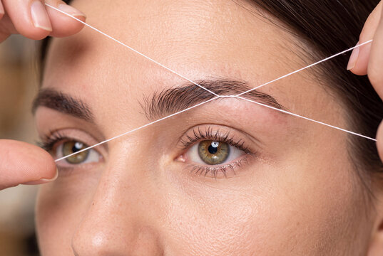 Closeup of a woman having her eyebrows shaped with thread, professional eyebrow threading technique