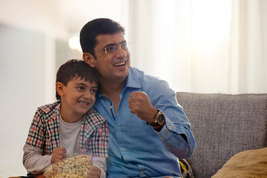 Father and son watching sports program in the television and eating popcorn