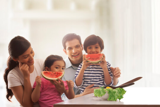 Children eating watermelon slice with their parents at kitchen table