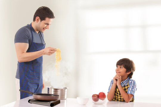 Father and son cooking noodles in kitchen