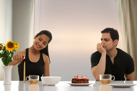 Young man looking at woman lighting candle at table with cake