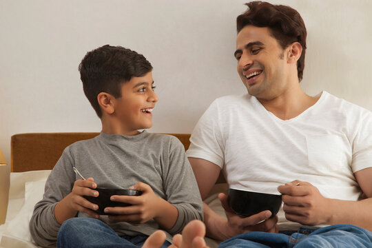 Father and young son having breakfast in bed