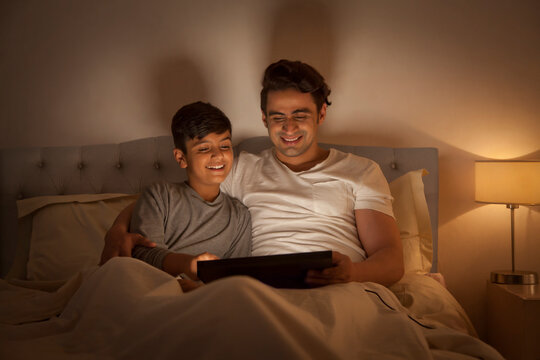 Father and son using digital tablet in bed