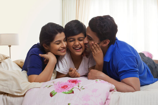 Smiling parents kissing son in bedroom