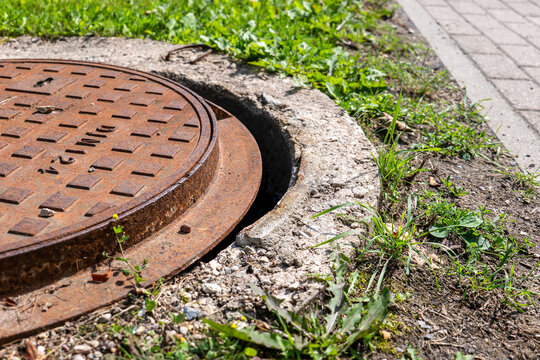 Dangerous Rusted Manhole Cover Sits Uneven Beside a Public Sidewalk