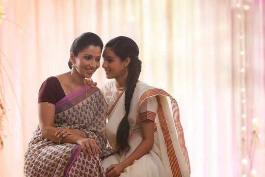 Smiling teenage daughter in sari whispering to mother