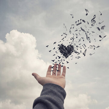 Open hand reaching up with musical notes turning into flying birds in cloudy sky