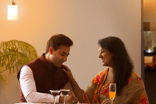 Mother and adult son sitting at table with soft drinks at party