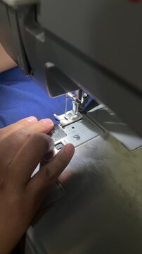 Close up of tailor hands sewing blue fabric using an electric sewing machine