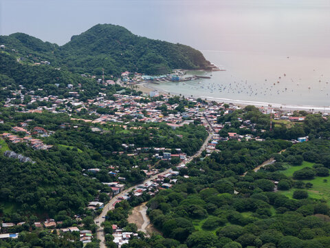 Aerial view of the coastal town of San Juan del Sur nestled between lush green hills and the Pacific Ocean, featuring a bay with small boats, San Juan del Sur, Rivas, Nicaragua.