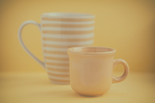 Close-up of two different yellow mugs in front of a yellow background