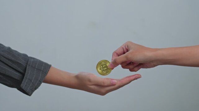 One person hand passes gold bitcoin coin into an open hand for illustrating cryptocurrency transaction