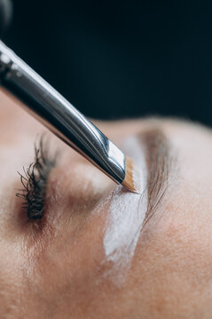 Permanent makeup artist applies white mapping paste to outline eyebrow shape before a cosmetic tattoo procedure in a professional beauty studio.