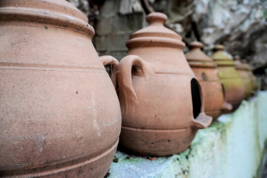 Close view of traditional terracotta clay jars in a row against a rocky wall. Handmade Mediterranean pottery