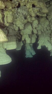 Several massive layered bell formations fill the frame beneath a rough rock ceiling at Cenote Zapote, Quintana Roo, Mexico.