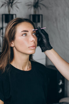 Beauty specialist applies eyebrow mapping paste before a permanent makeup procedure, preparing the client for precise eyebrow tattooing in a professional salon.