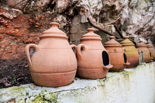 A row of handmade terracotta clay pots with lids by a rock wall in Turkey. Traditional Mediterranean pottery jars