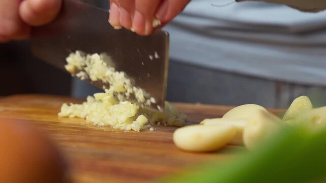 Close-up of hands mincing garlic on wooden board