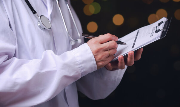 Focused professional doctor manages daily medical administration workflow while writing patient record on clipboard with stethoscope