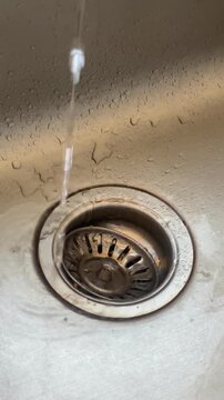 Water running from tap into a stainless steel sink drain