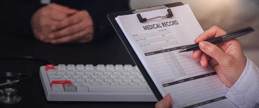 Professional clinician manages medical administration workflow with focused care while holding pen on clipboard document near patient