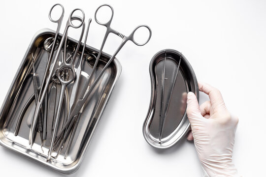 Hand in white glove is holding sterile surgical instruments and tools - scalpels, scissors and others - in a stainless tray, top view