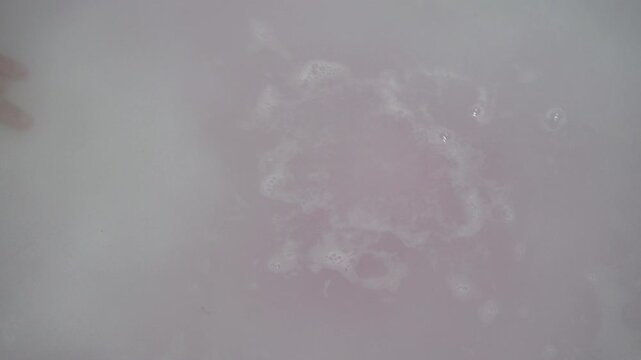 A child's hand drops a pink bath bomb into the bath, The process of dissolving a pink effervescent ball in a bath close-up