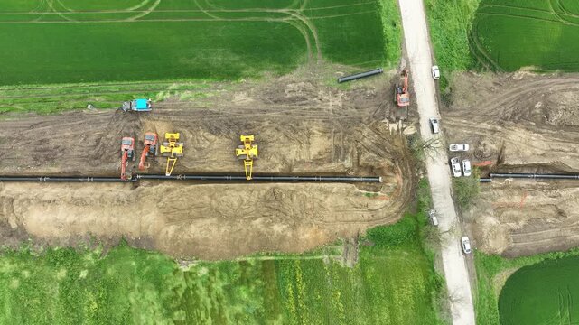 Aerial view of a major pipeline construction project. Heavy machinery including excavators and pipelayers install a new gas line in a rural field. Industrial energy infrastructure development.
