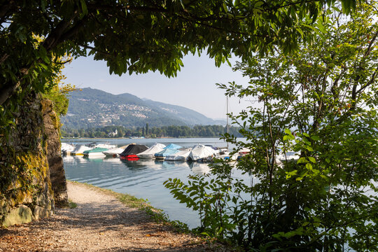 A narrow path leading out of the woods and down to a lakeside harbour. A romantic landscape in Caslano, Switzerland