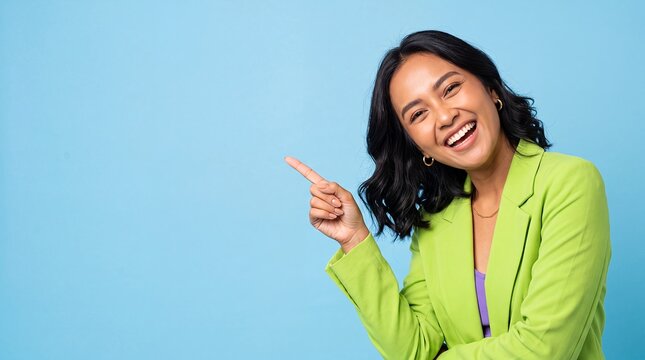 pointing asian woman left copyspace blue background laughing blazer cheerful Model in a lime jacket gestures toward open space with one finger for product promotion messaging and advertising layouts