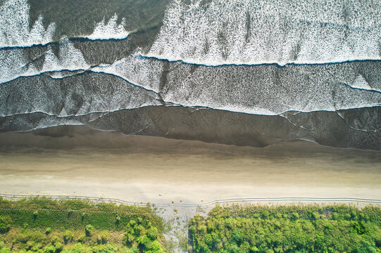 Aerial view of Quizala beach with white waves crashing on the sandy shore and lush green vegetation bordering the coastline in San Rafael del Sur, Managua, Nicaragua.