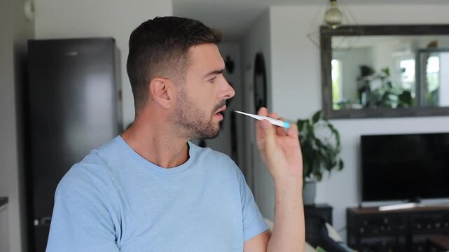 Sick man checking electronic mouth thermometer and reacting to high fever