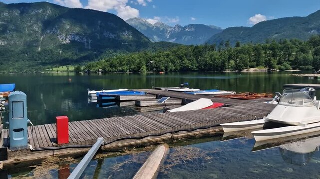 Moored Boats and Kayaks by Wooden Dock on Lake Bohinj Slovenia on Sunny Summer Day