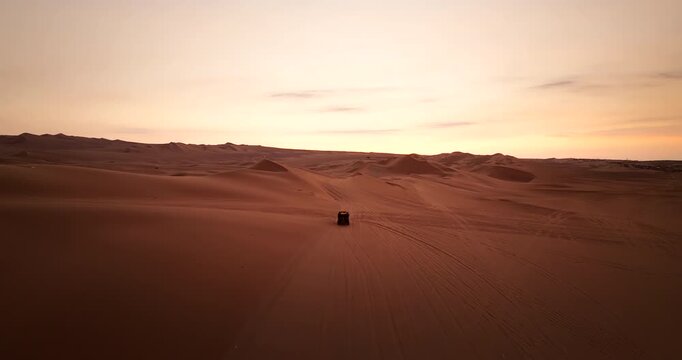 Drone view of dune buggy vehicle on sand dune with tire track at dusk in Huacachina, Peru. Aerial forward, copy space
