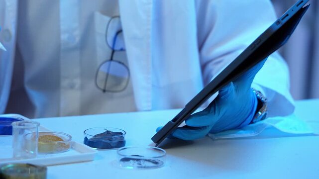 Hand of researcher holding stylus pen and writing data on digital tablet computer with petri dish sample in laboratory