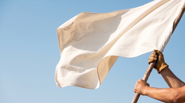 A person's gloved hands hold a white flag waving in the wind against a clear, bright blue sky.