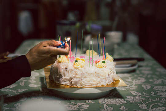 Close up of hand using a lighter to light candles on white coconut birthday cake.